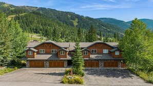 A two-story wooden cabin with a garage, surrounded by a mountainous landscape.