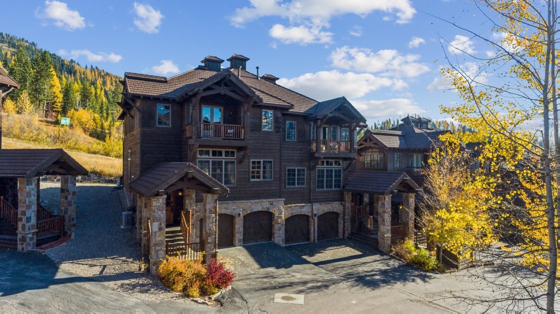 A large, multi-story wooden house with a stone entrance and multiple balconies.