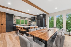 A modern kitchen with a central island, bar stools, and a dining table with grey upholstered chairs. - Boot Dryers | Ski-in/out | Hot Tub (Whitefish)