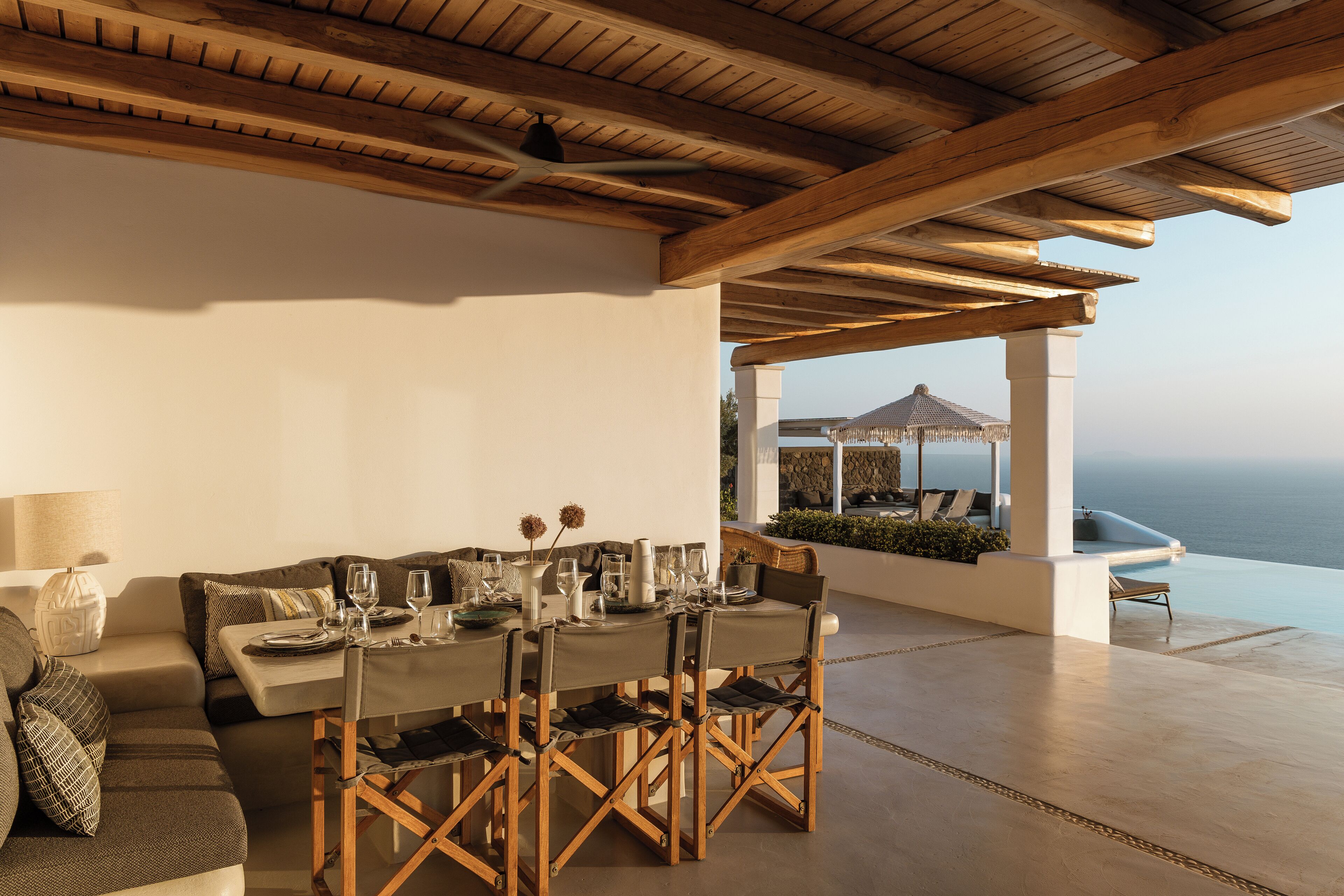Un coin repas avec une table dressée pour six personnes, des poutres en bois au plafond et une vue sur la mer.