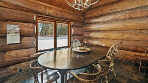 A log cabin interior with a round dining table, wooden chairs, a chandelier, and a calendar on the wall.