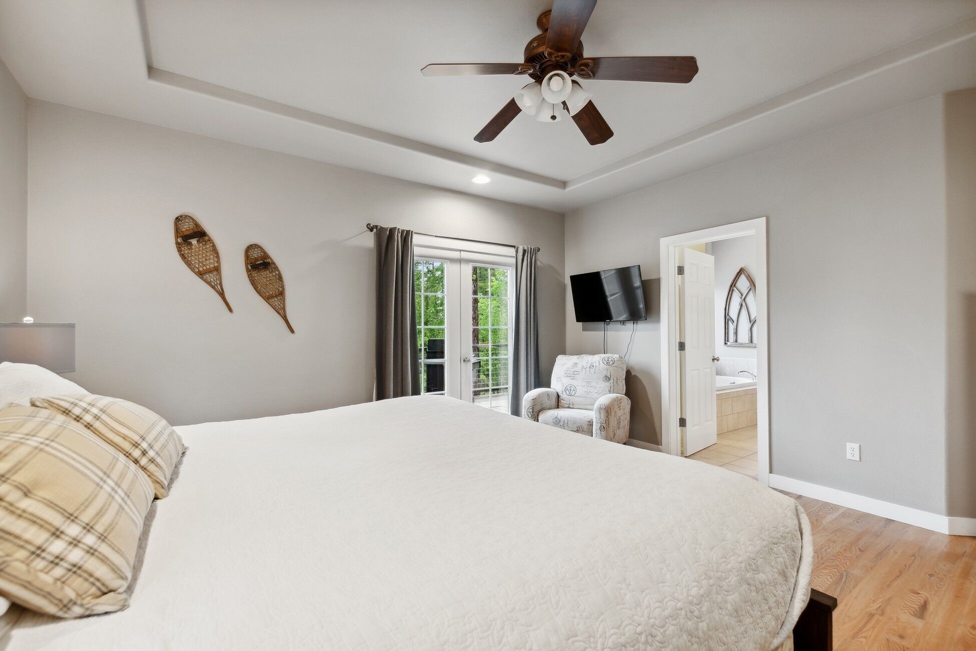 Quarto com uma cama grande, um ventilador de teto, televisão na parede e vista exterior por uma porta deslizante.
