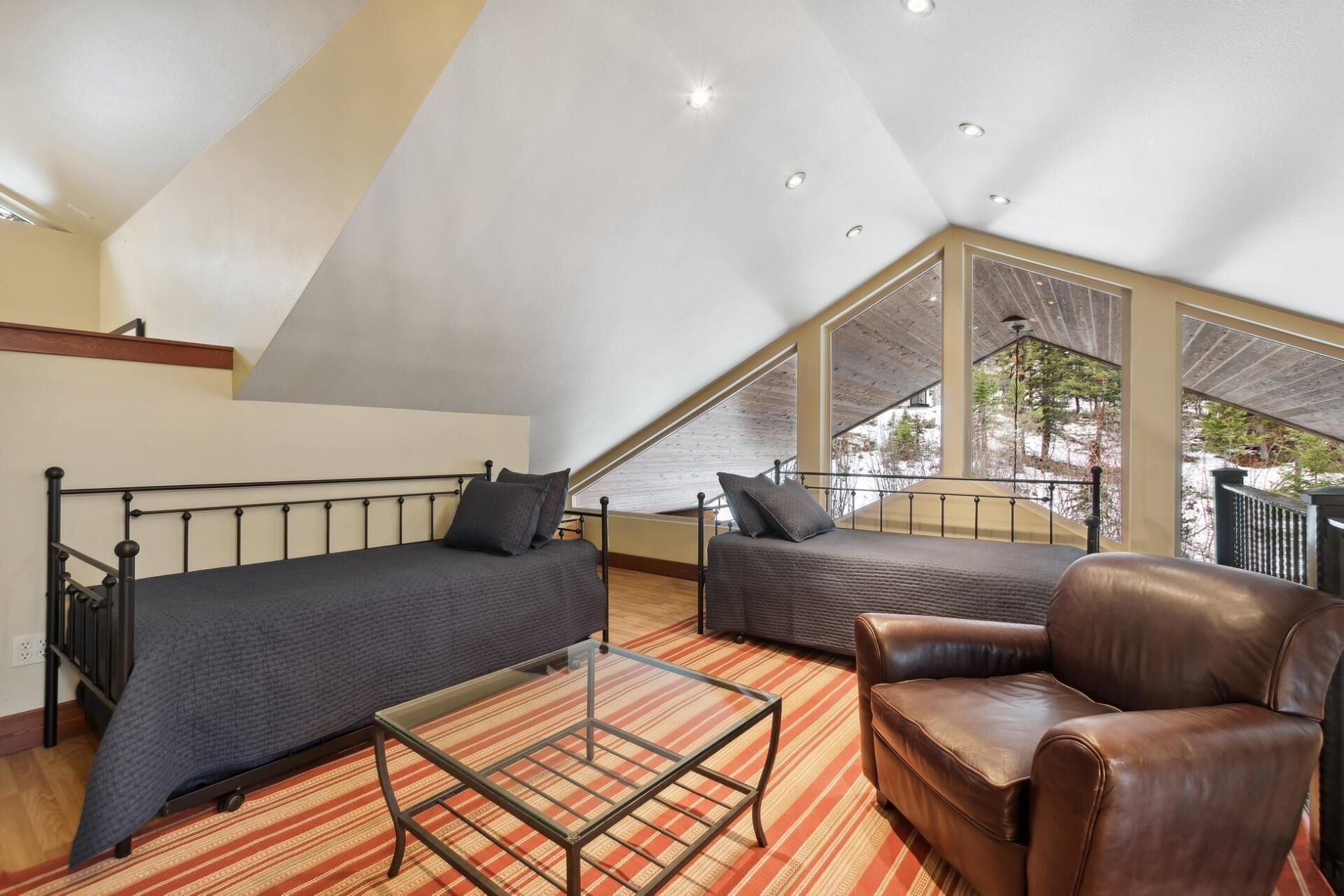 Un dormitorio tipo loft con techo inclinado, una cama, un sofá, un sillón de cuero y una mesa de centro de vidrio.