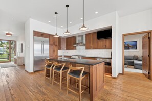 Una cocina moderna con una isla central, taburetes de madera, electrodomésticos de acero inoxidable e iluminación colgante.