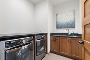 A compact laundry room with two front-loading washing machines, a wooden cabinet, and a black countertop.