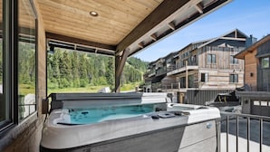 Un jacuzzi sur un balcon offrant une vue sur une région montagneuse et un immeuble à plusieurs étages.