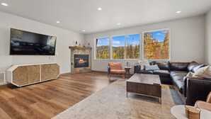 Un salon moderne doté d’une cheminée, d’un canapé en cuir et de grandes fenêtres offrant une vue sur le paysage automnal.