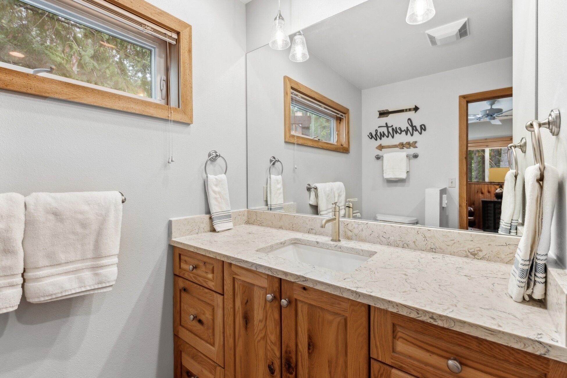 A bathroom with a wooden vanity, a sink, and a mirror. There are towels hanging on the wall and a window with blinds.