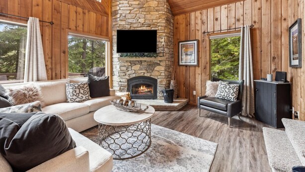 L’intérieur chaleureux d’un chalet avec une cheminée en pierre, des murs en bois et un coin salon confortable.