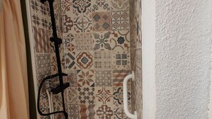 Eine Dusche mit schwarzem Duschkopf, weißer Haltegriff und gefliesten Wänden mit verschiedenen Mustern.