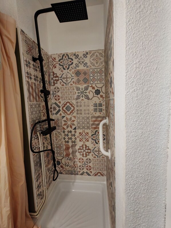 Eine Dusche mit schwarzem Duschkopf, weißer Haltegriff und gefliesten Wänden mit verschiedenen Mustern.