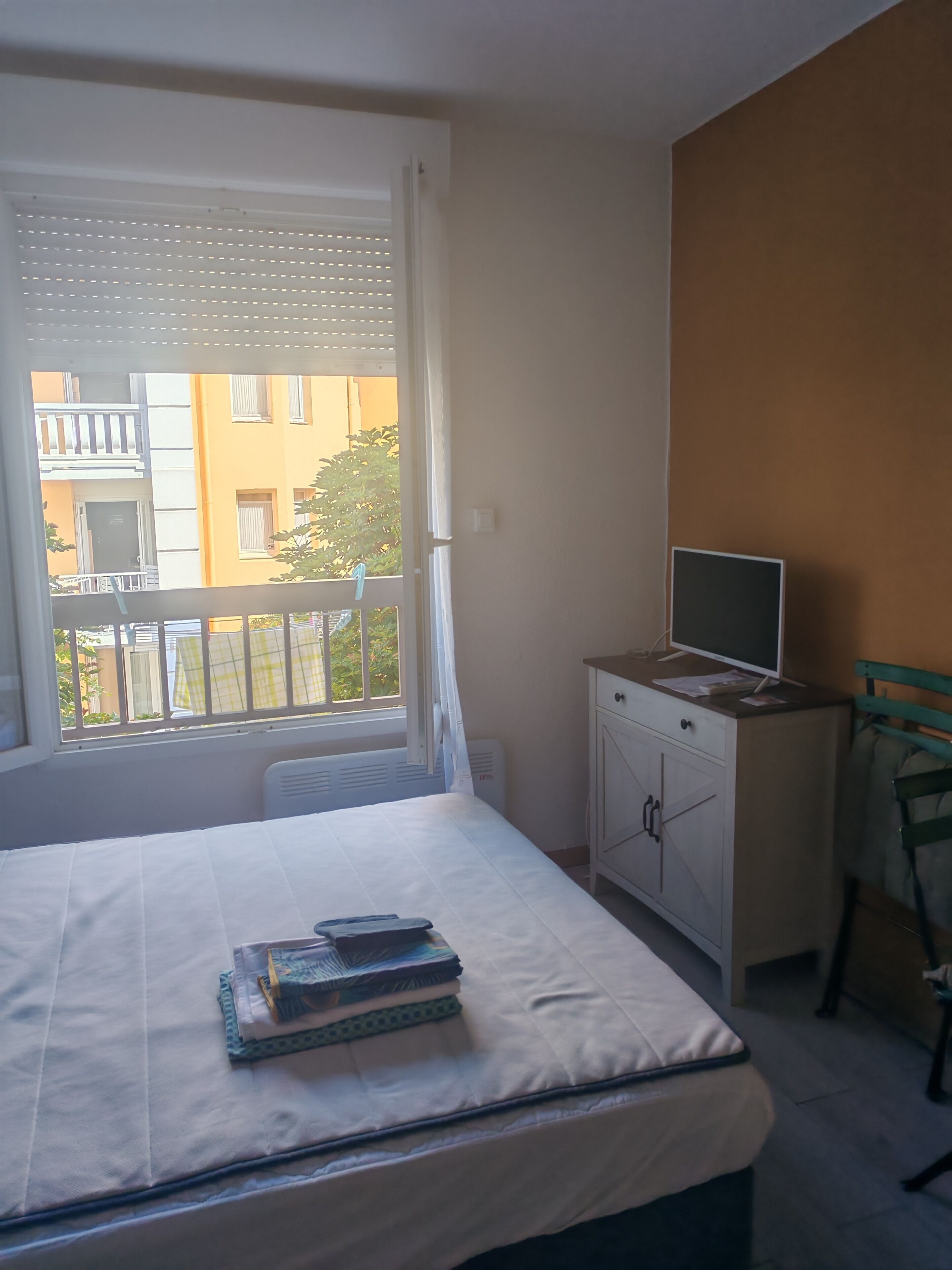 Een slaapkamer met een bed, een bureau met een computer en een raam met zonwering.