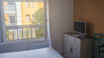 Een slaapkamer met een bed, een bureau met een computer en een raam met zonwering.