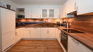 A kitchen with white cabinets, a wooden countertop, and a backsplash with a coastal scene. - Herzlich Willkommen in der Wohnung "diekleev"! (Büsum)