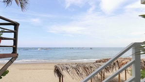 A beach view with a wooden staircase leading down to the sand, a thatched roof structure, and boats in the water. - w* | Fascinating loft with Spectacular Ocean View (Máncora)