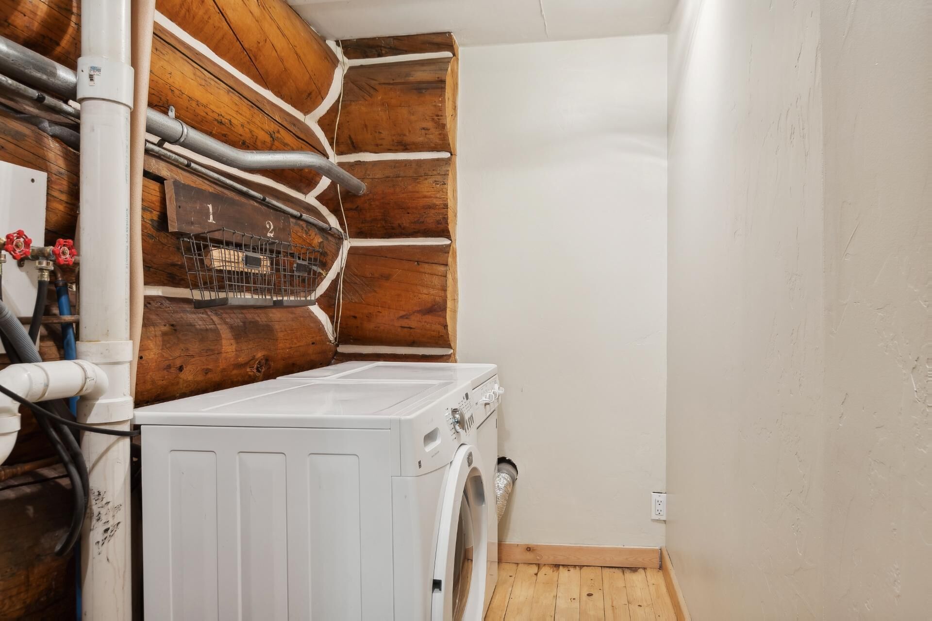 A laundry room with a white washing machine, wooden cabinets, and visible plumbing.