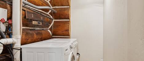 A laundry room with a white washing machine, wooden cabinets, and visible plumbing.