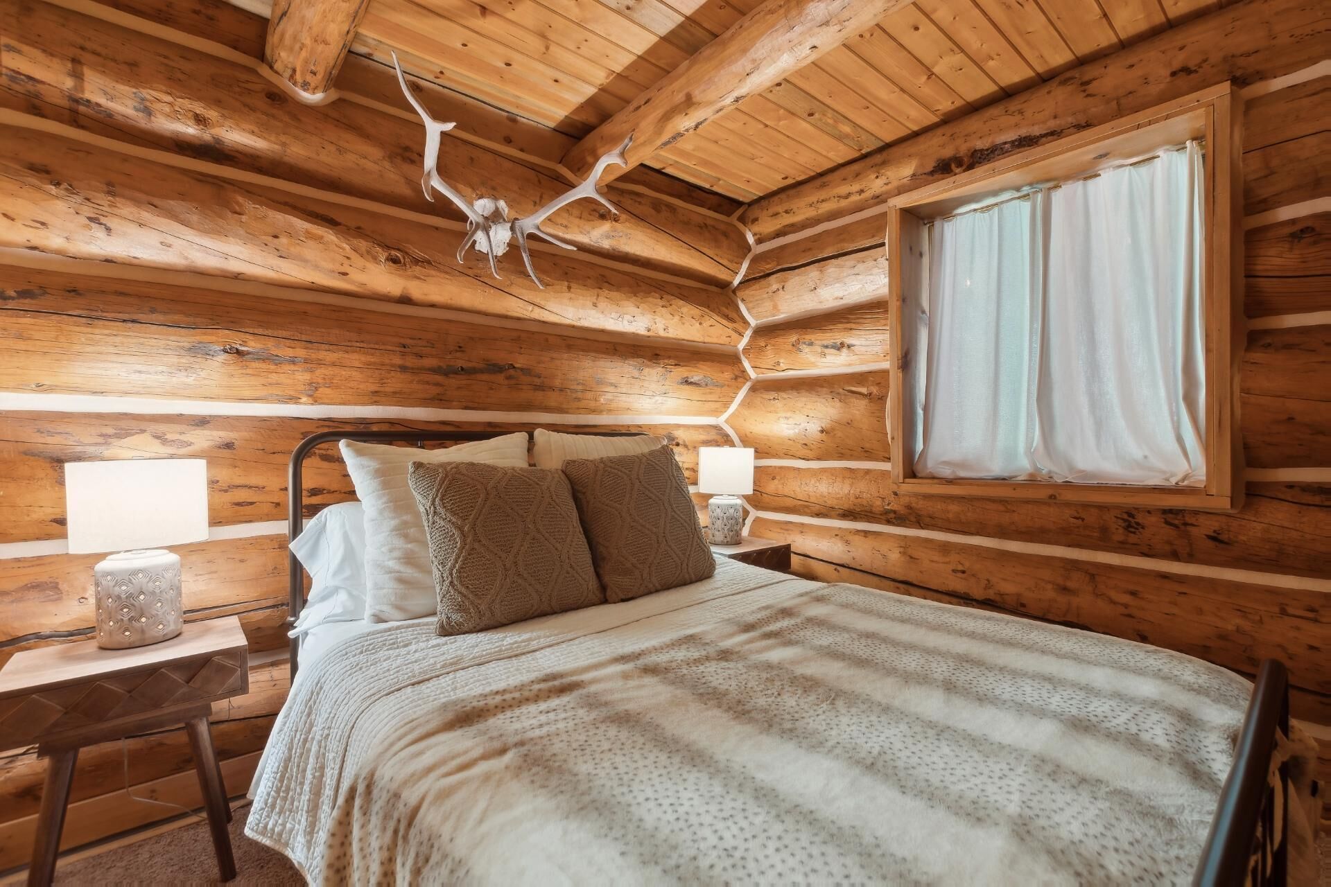 En stuga med träpanel, ett rum med en säng, två sänglampor och ett fönster med gardiner.