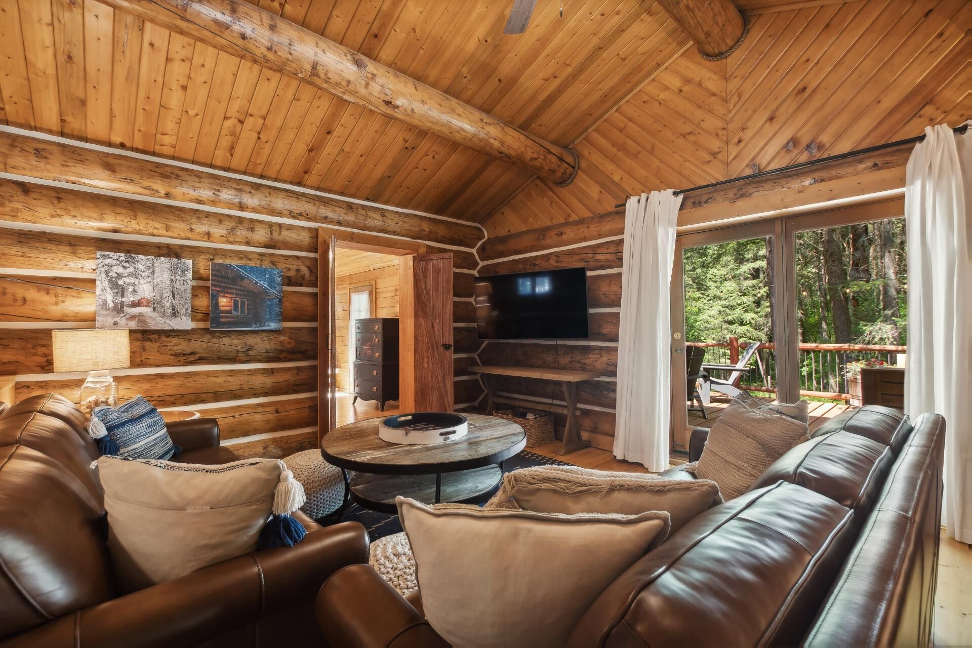 Ein gemütliches Blockhaus-Interieur mit Ledersofa, rundem Couchtisch und einem flachbildfernseher an der Wand.