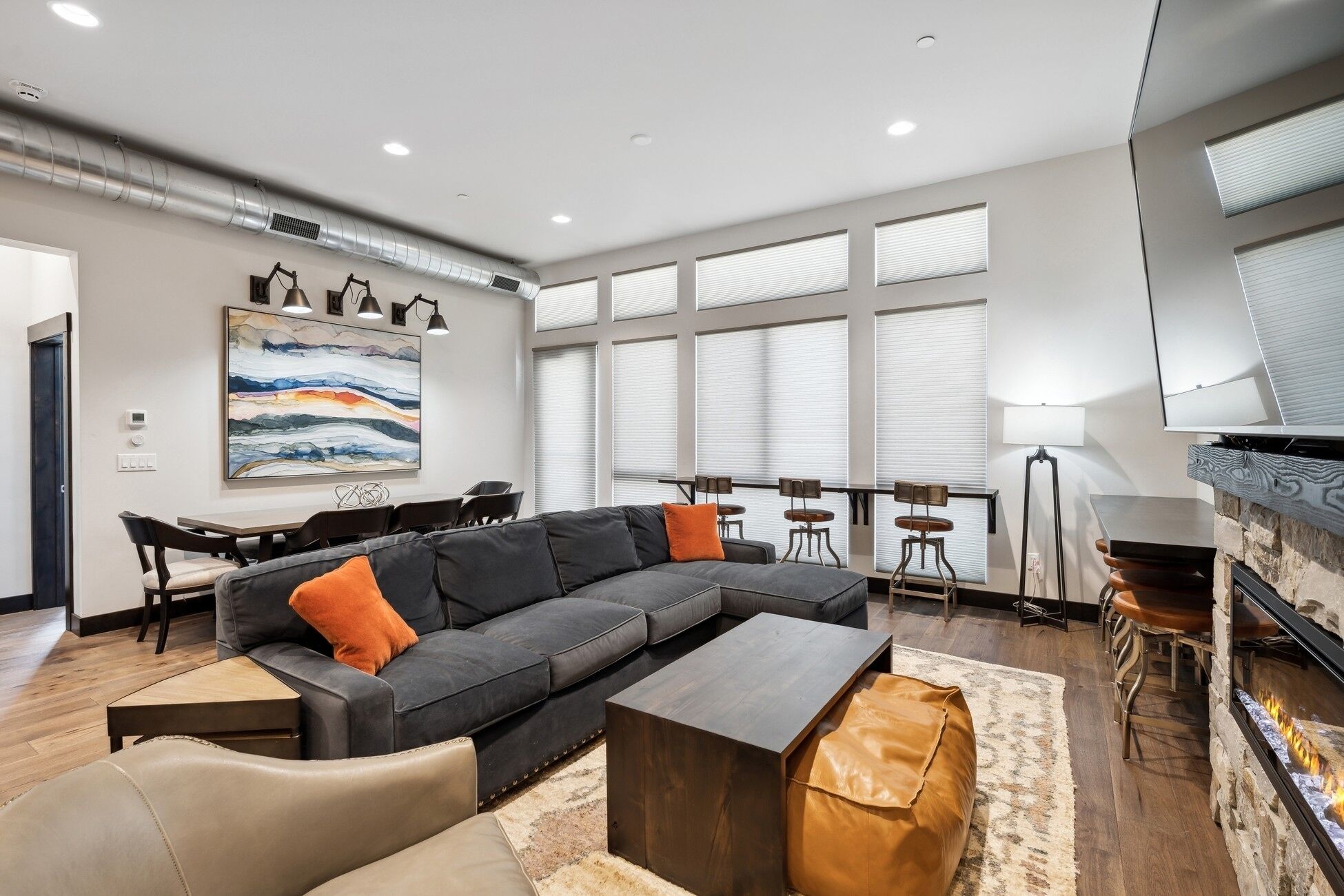 Un salon moderne avec un canapé d’angle, une table basse, une cheminée et une grande fenêtre équipée de stores.