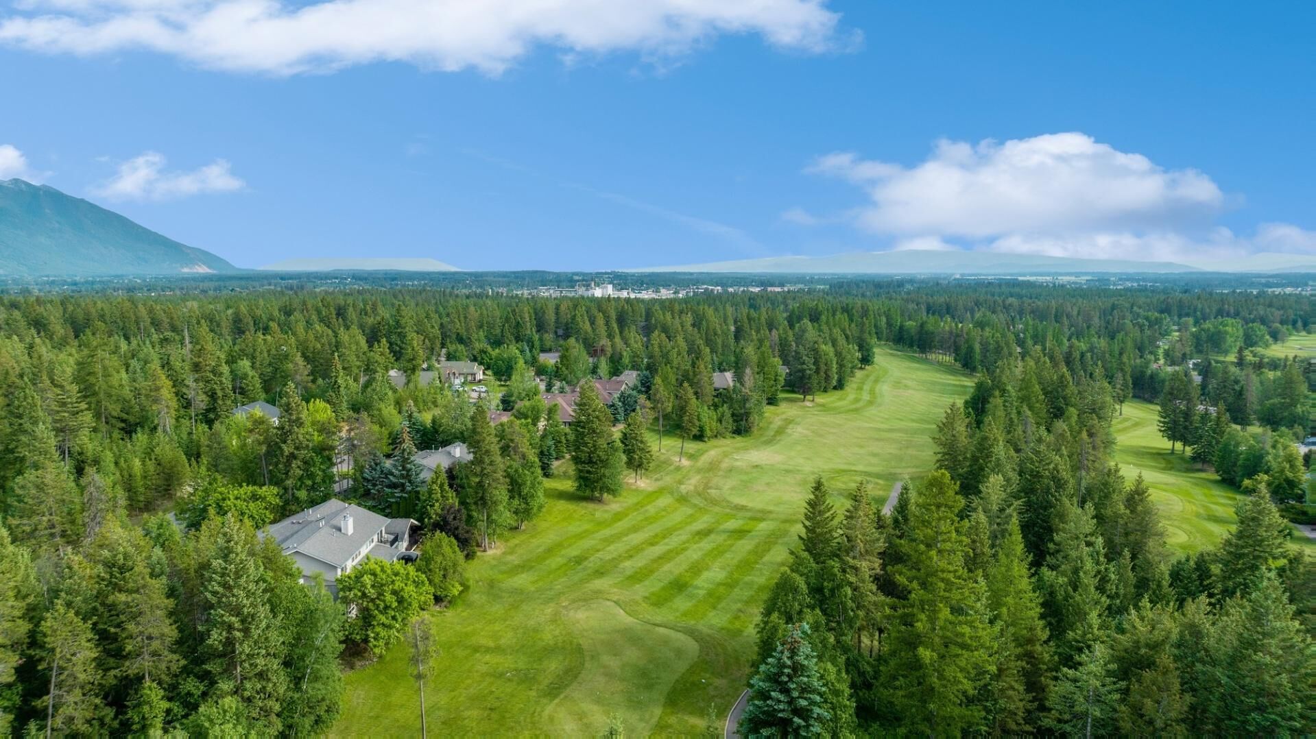 En golfbane omgivet af tætte skove og parcelhuse.