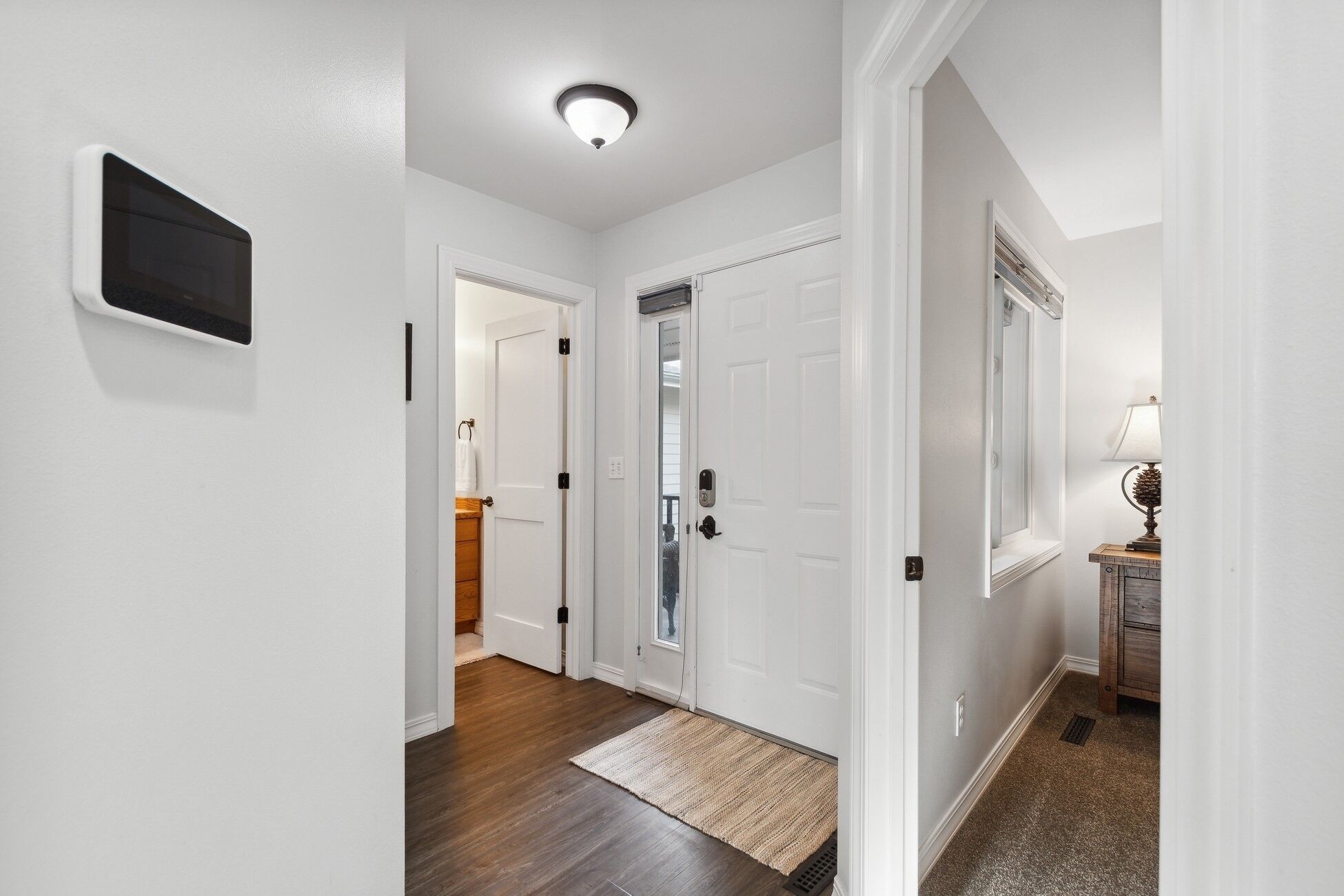 A hallway with white walls, a wooden floor, and a door with a mirror.