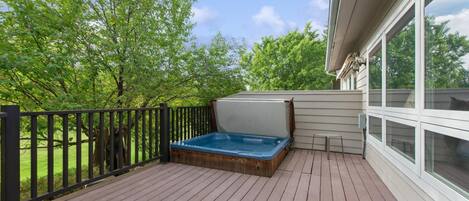 A wooden deck with a hot tub, a small table, and a railing.