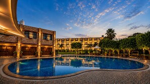 Una piscina de borde curvo, rodeada por una zona pavimentada y un edificio con varias ventanas y balcones.
