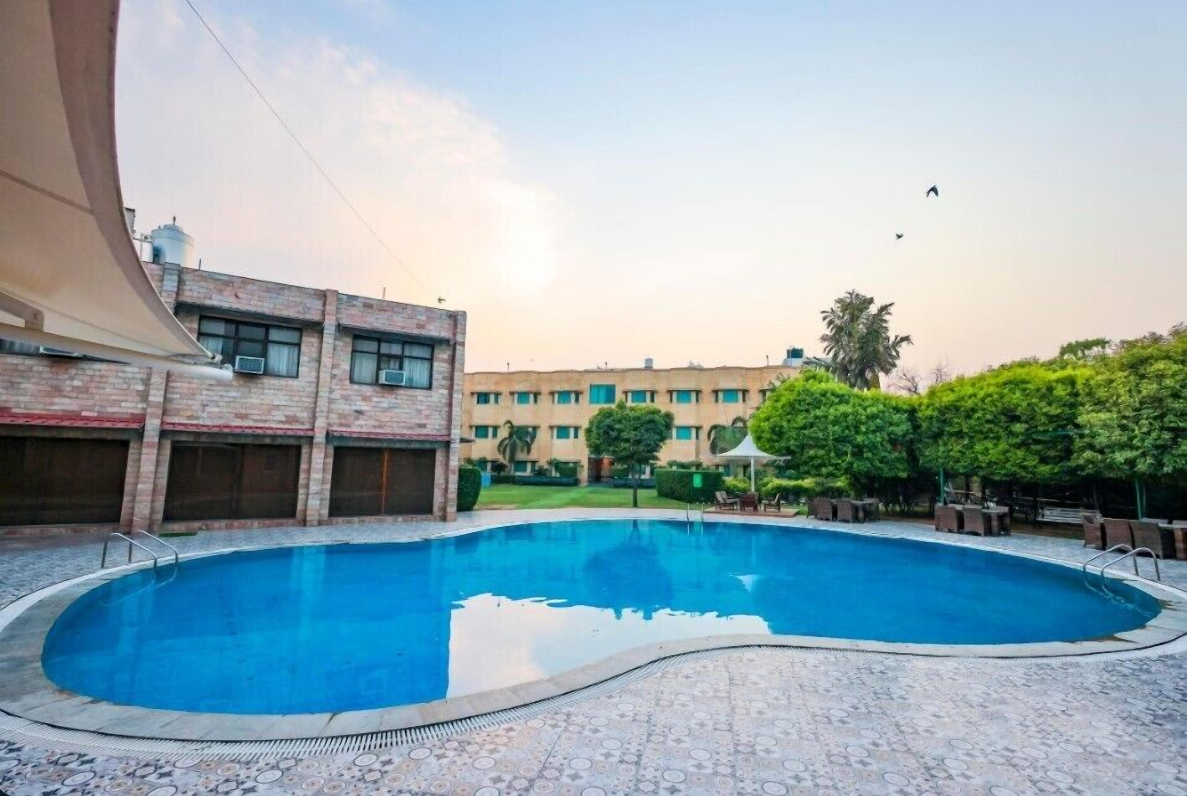 A swimming pool with a tiled deck, surrounded by a building with multiple windows and a flat roof.