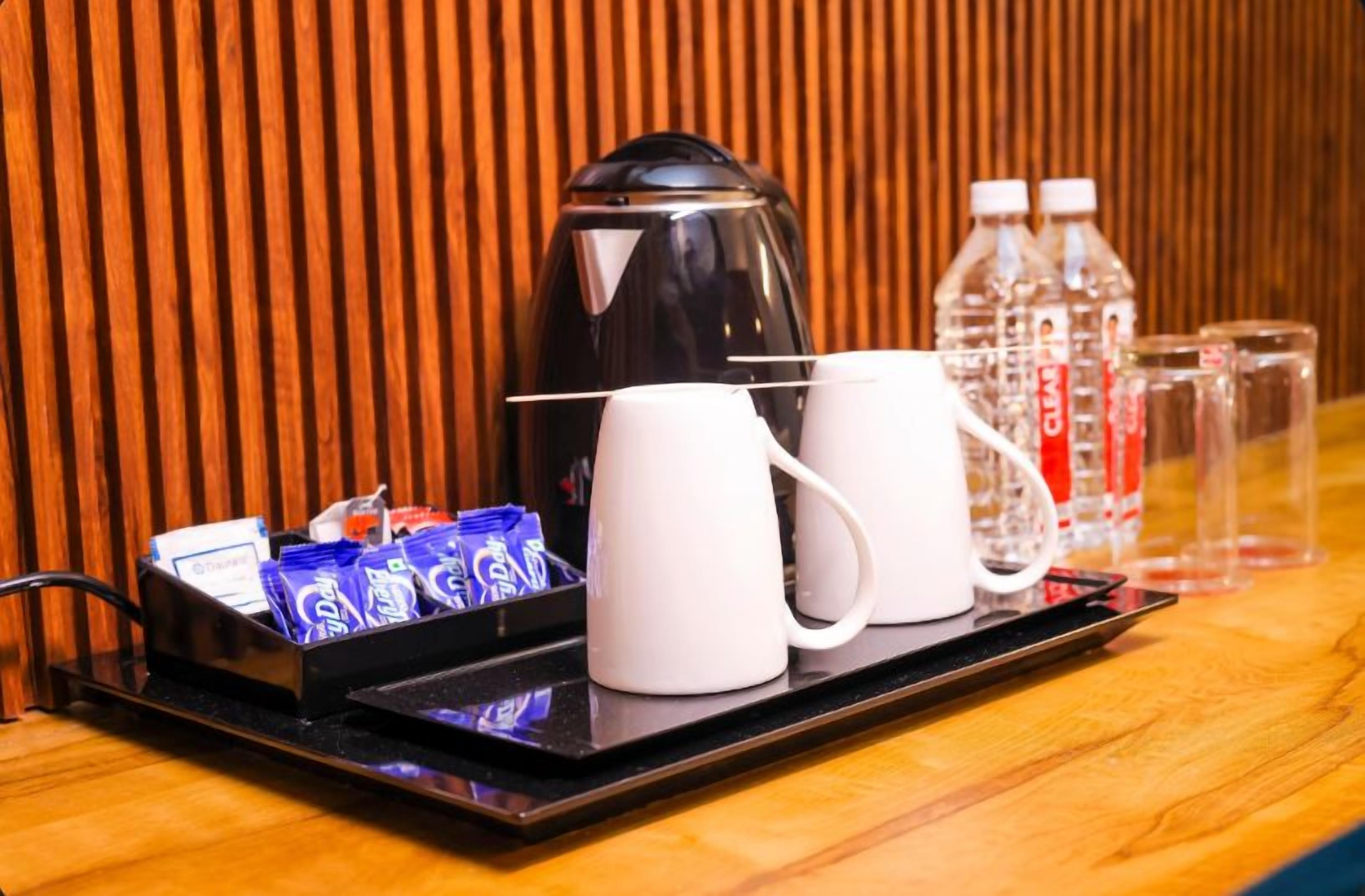 A tray with a coffee maker, two white mugs, and a water bottle on a wooden table.