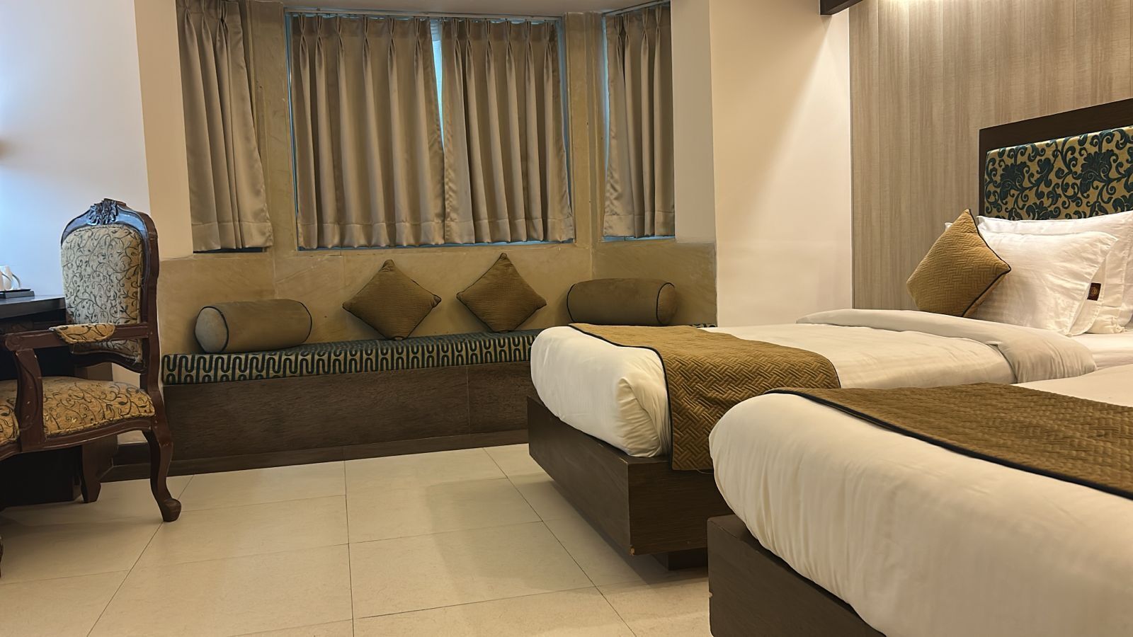 A hotel room with two beds, a sofa, a chair, and a window with curtains.