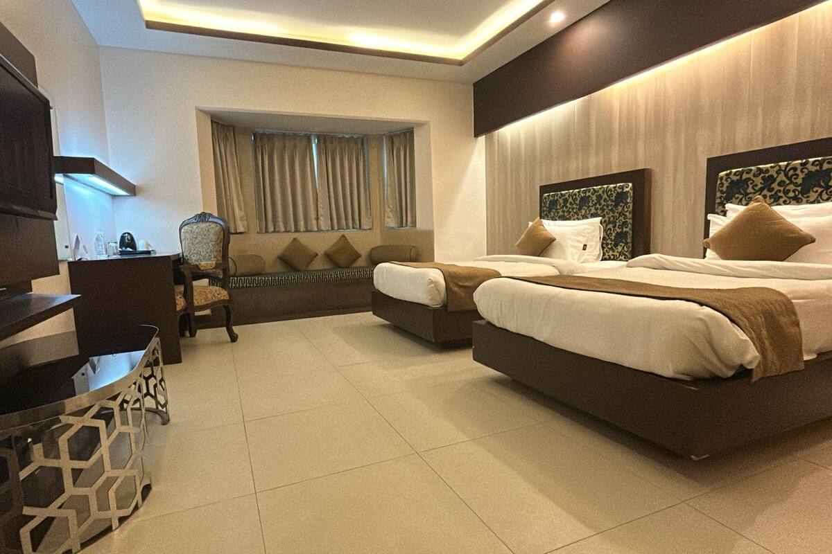 A hotel room with a TV, a sofa, a chair, two beds, and a window with curtains.