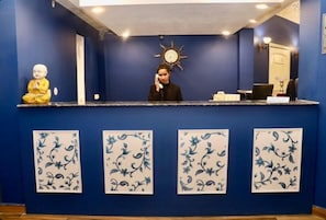 Un mostrador de recepción con pared azul, una estatua de Buda y decoración floral en la pared.
