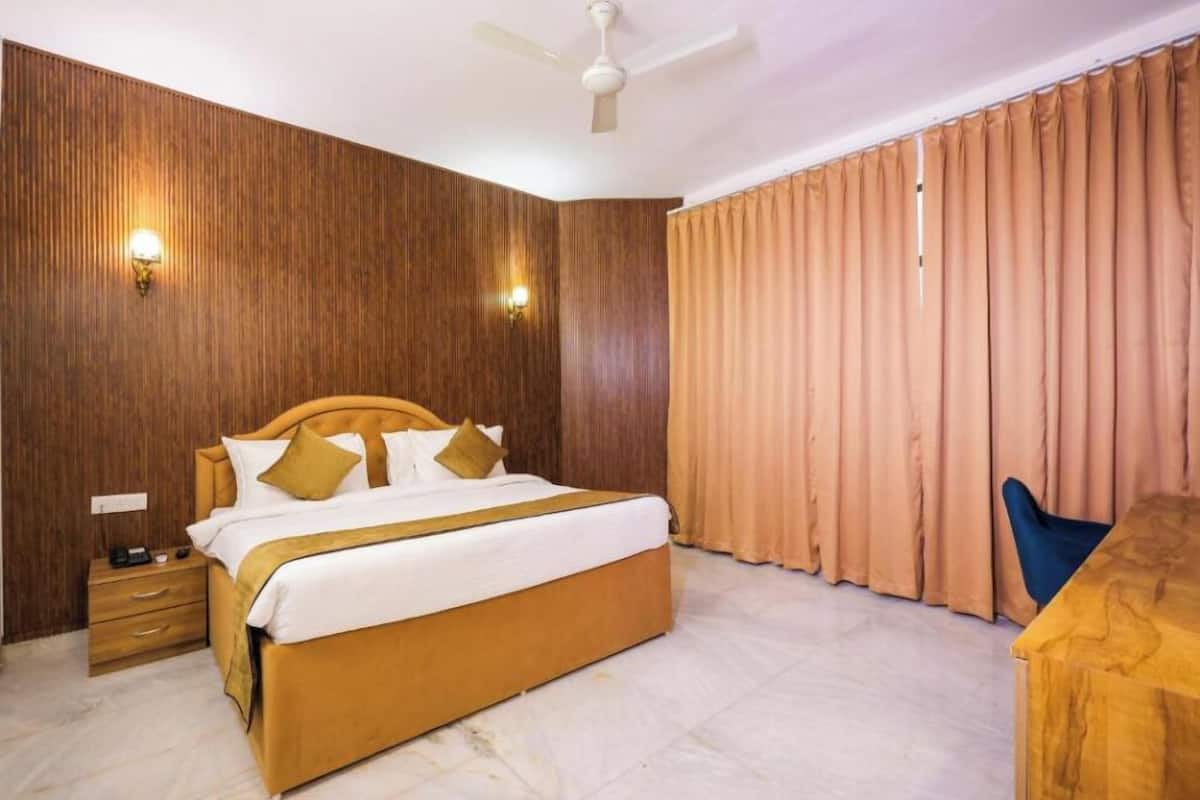 A hotel room with a wooden headboard bed, a nightstand, a desk, and a large window with curtains.