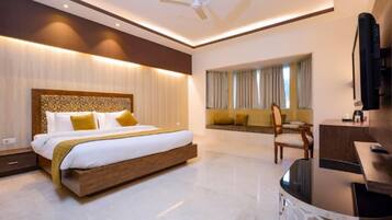 A modern hotel room with a large bed, a seating area with a sofa and chairs, a dining table, and a television.