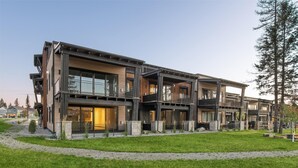 A modern multi-story building with balconies, large windows, and a well-maintained lawn. - Penthouse w/ Hot Tub, Fireplace and Firepit (Whitefish)