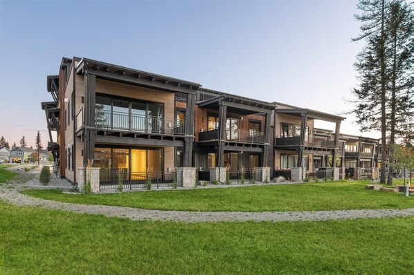 Een modern, meerhoog gebouw met balkons, grote ramen en een verzorgd gazon.