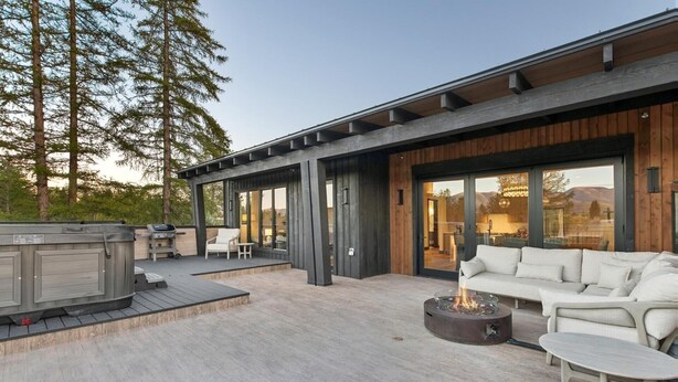 A modern outdoor patio with a fire pit, seating area, and a hot tub. - Penthouse w/ Hot Tub, Fireplace and Firepit (Whitefish)