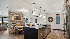 A modern kitchen with a central island, wooden flooring, and pendant lighting. - Ski Room | Mountain Views | Hot Tub (Whitefish)