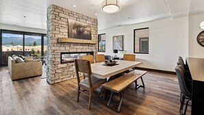 A spacious dining area with a stone fireplace, wooden furniture, and large windows offering a view of the mountains. - Ski Room | Mountain Views | Hot Tub (Whitefish)