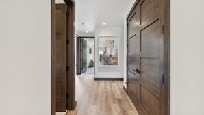A hallway with wooden flooring and doors, leading to a room with a framed picture on the wall. - Ski Room | Mountain Views | Hot Tub (Whitefish)
