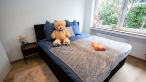 A bedroom with a bed, a teddy bear, and a window with a view of trees. - Traumhafte Stadtwohnung (Duisburg)