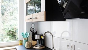 A kitchen with a modern design, featuring a black range hood, a coffee maker, and a window with a view of trees. - Traumhafte Stadtwohnung (Duisburg)