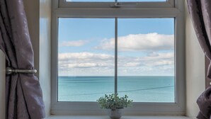 Ein Fenster mit Meerblick, Vorhängen und einer kleinen Pflanze auf der Fensterbank.