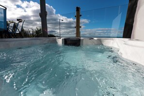 Ein Whirlpool mit klarem Wasser, umgeben von einem Poolbereich mit Liegestühlen und Blick auf den Himmel.
