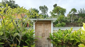 A wooden door with a stone pathway leading to it, surrounded by lush greenery. - Alam Cottage Uluwatu (Pecatu)