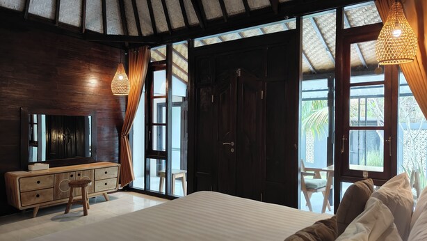 A bedroom with a large bed, wooden furniture, a TV, and a view of the outdoors. - Alam Cottage Uluwatu (Pecatu)