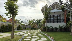 A garden with a stone pathway leading to a house with large windows and a balcony. - Alam Cottage Uluwatu (Pecatu)