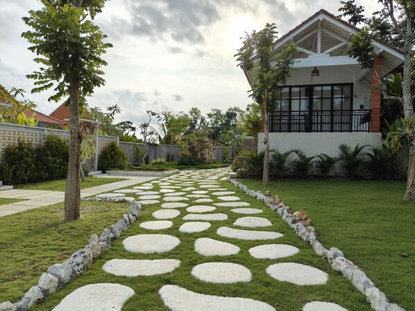 Un jardí amb un camí de pedra que condueix a una casa amb grans finestres i un balcó.