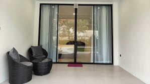 A modern room with a sliding glass door leading to an outdoor area, featuring a wicker chair and a small table. - Alam Cottage Uluwatu (Pecatu)